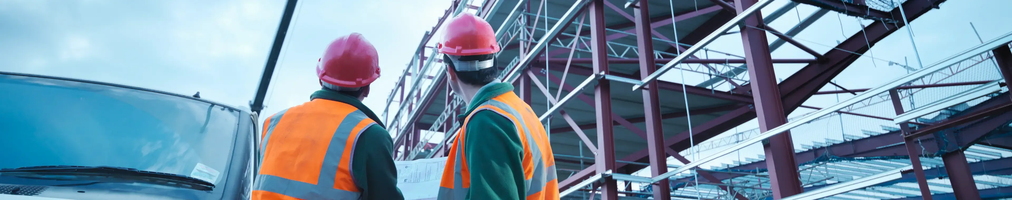 Workmen watching crane lifting roof panels onto steel construction frame on building site